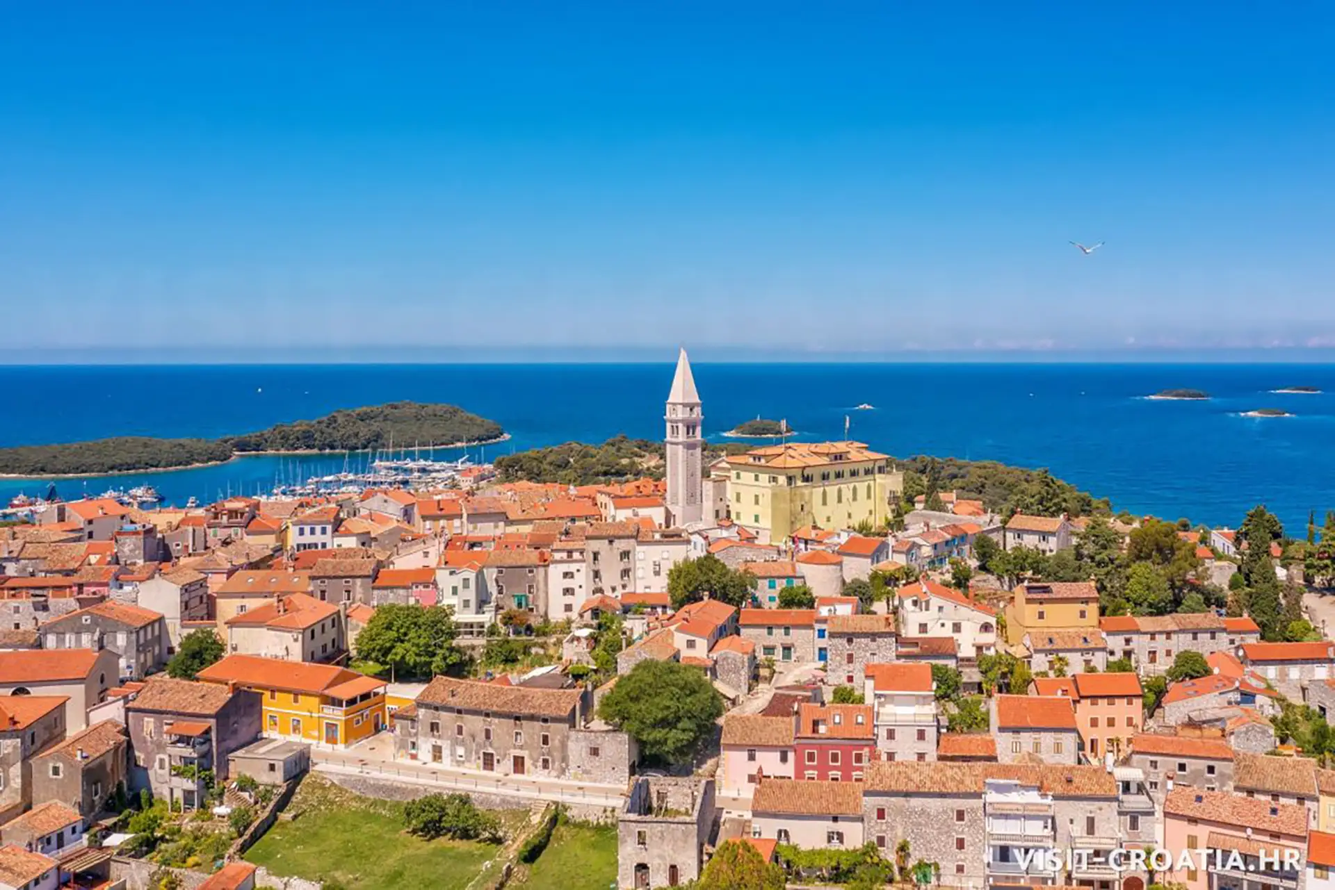 Copyright: visit-croatia.hr An aerial view of Vrsar, Croatia, showcasing its charming coastal town with terracotta rooftops clustered around the iconic bell tower of the Church of St. Martin.