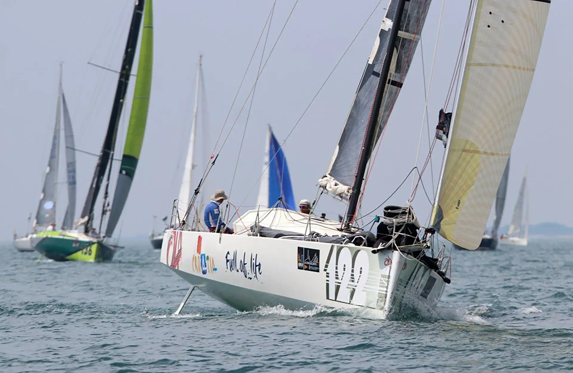 A sailing regatta featuring a white Class 40 sailboat with 'Croatia Full of Life' written on its side, co-skippered by Ivica Kostelić, racing on a blue sea towards their 2018 victory.