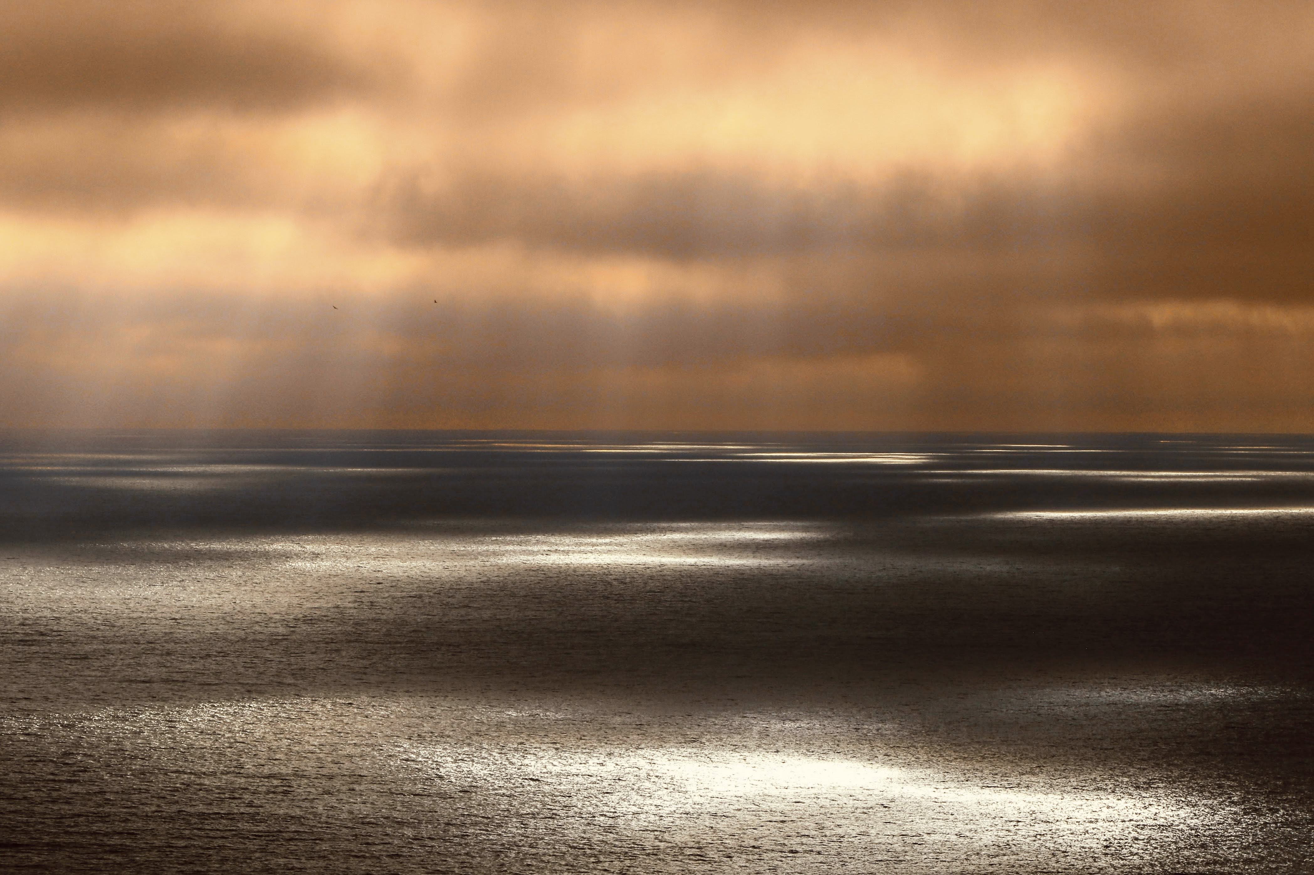 Sunrise over calm waters with a sailboat on the horizon, offshore sailing adventure.