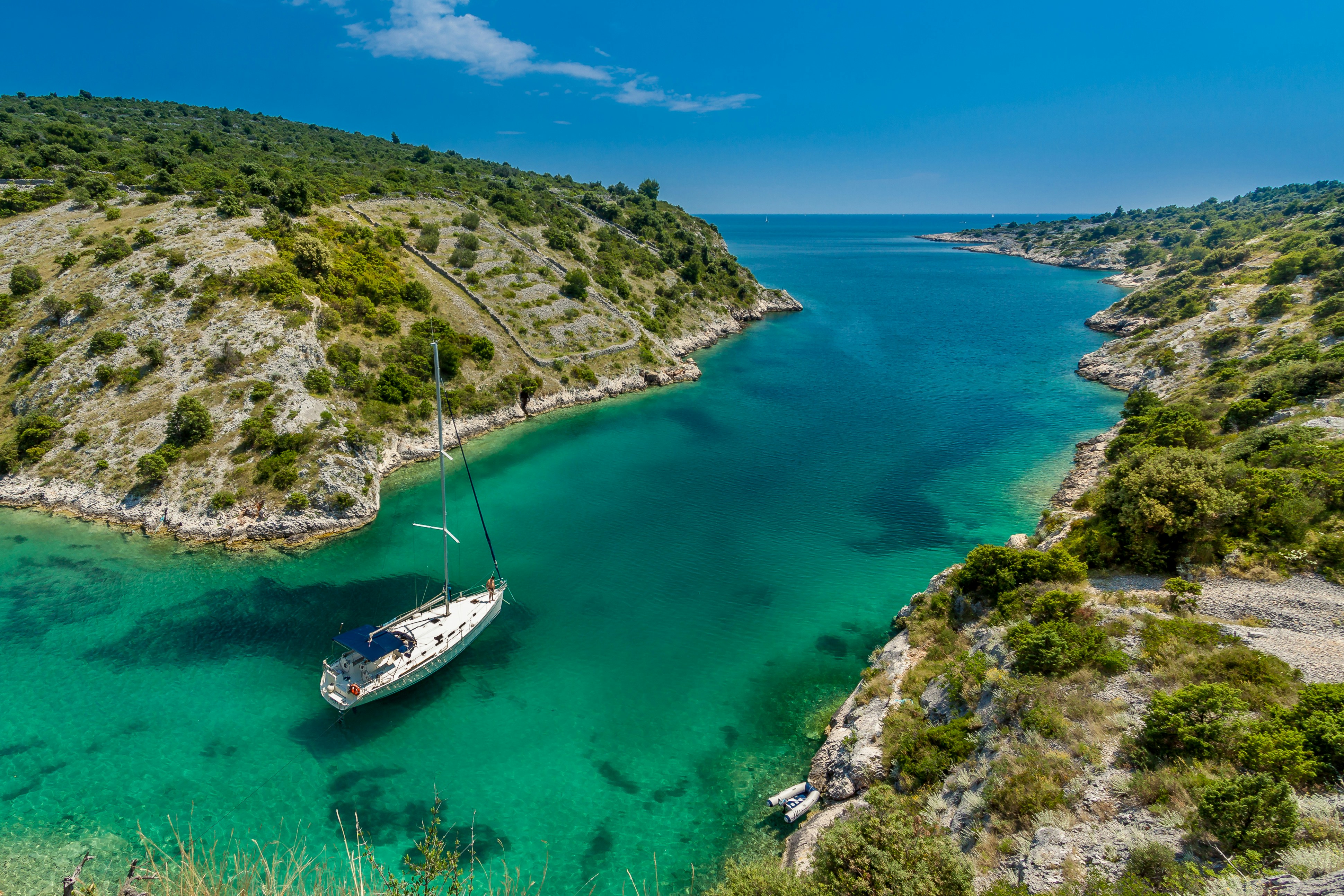 Aerial view of a sailboat anchored in a secluded cove with crystal-clear turquoise water.